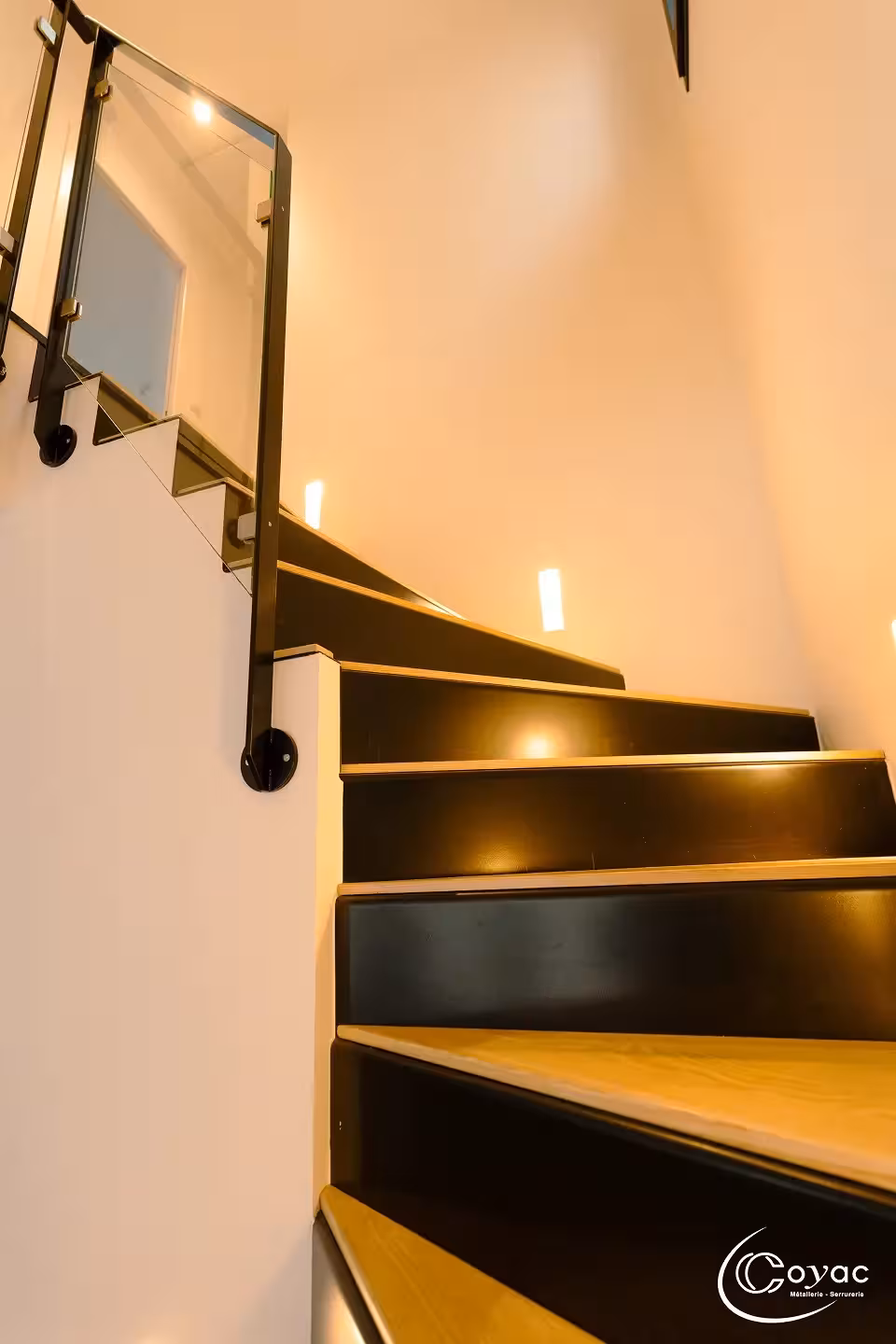 Vue ascendante d'un escalier sur-mesure métal et bois à Savenay, garde-corps vitré et main courante en acier noir, signé Coyac